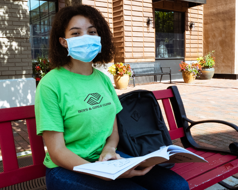 boys and girls club girl wearing mask reading a book