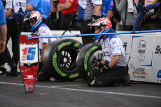 Pit crew kneeling on ground w/ guayule tire